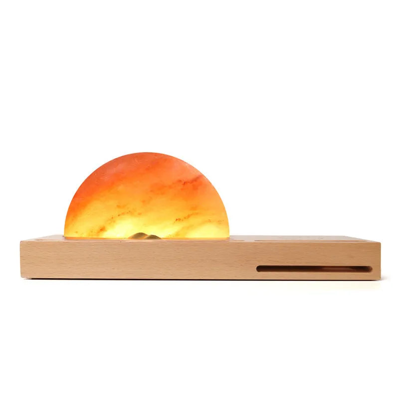 Wooden-based table lamp with a glowing orange Himalayan salt shade, wirelessly charging a mobile phone on its surface.