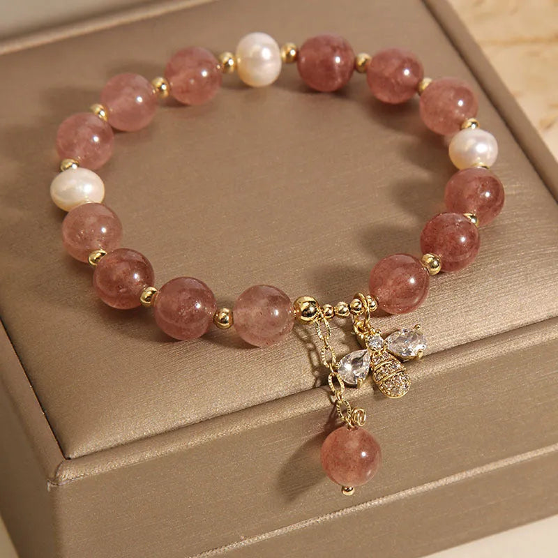 Women's pink strawberry quartz and white freshwater pearl bracelet with zircon details on wrist.