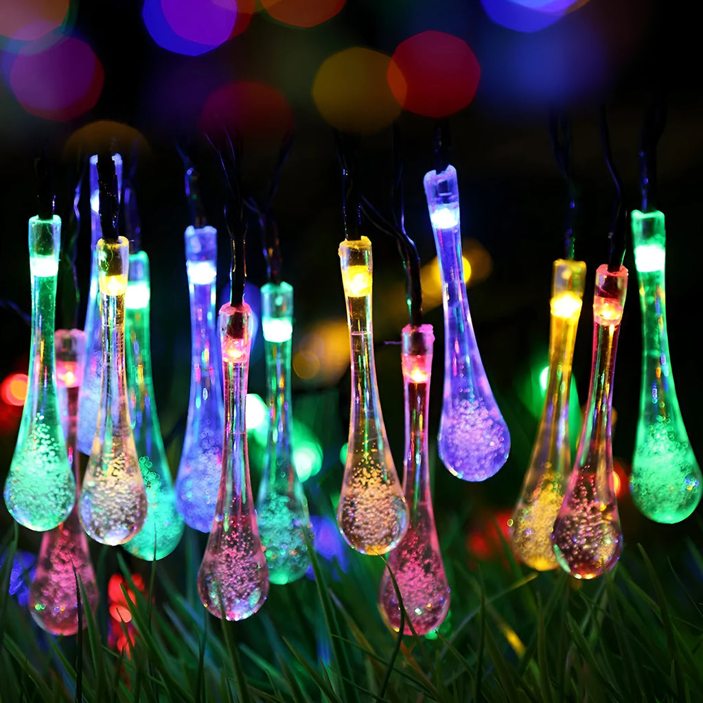 String of solar-powered bubble drop LED lights with a solar panel and ground spike for outdoor garden use.