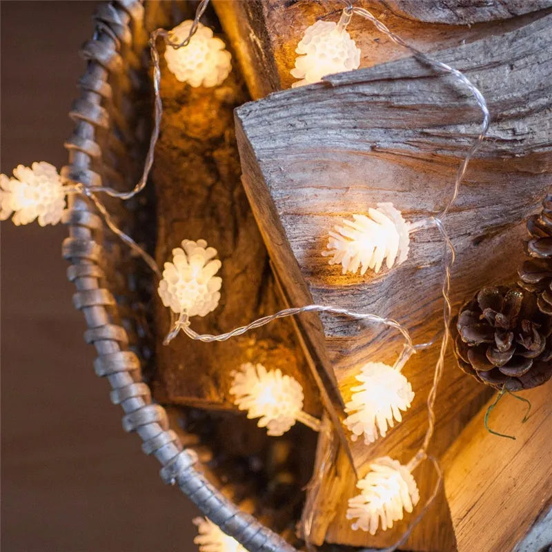 Warm white LED pine cone string lights draped over a surface, showing plastic shell details and battery pack.