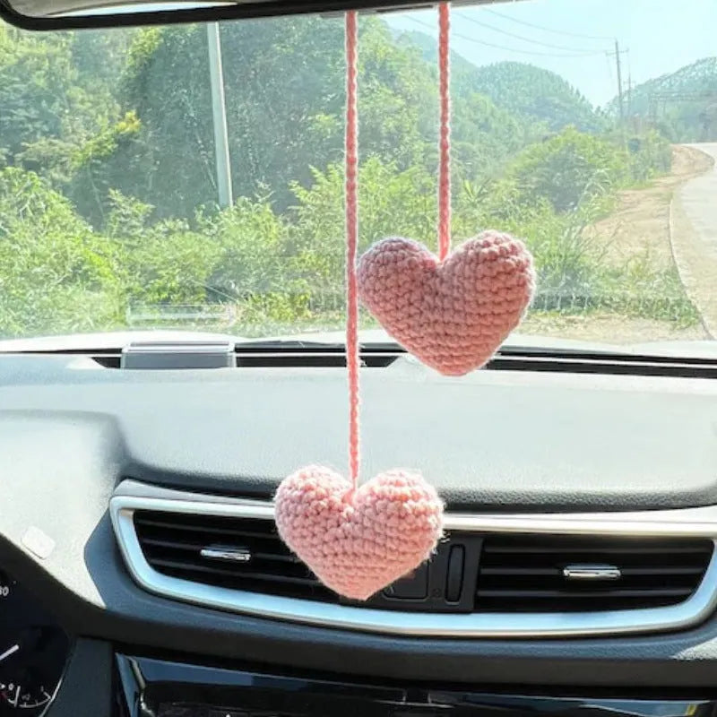 Green and white crocheted car plant decoration with hanging rope on a car dashboard.