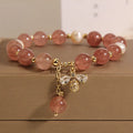 Women's pink strawberry quartz and white freshwater pearl bracelet with zircon details on wrist.