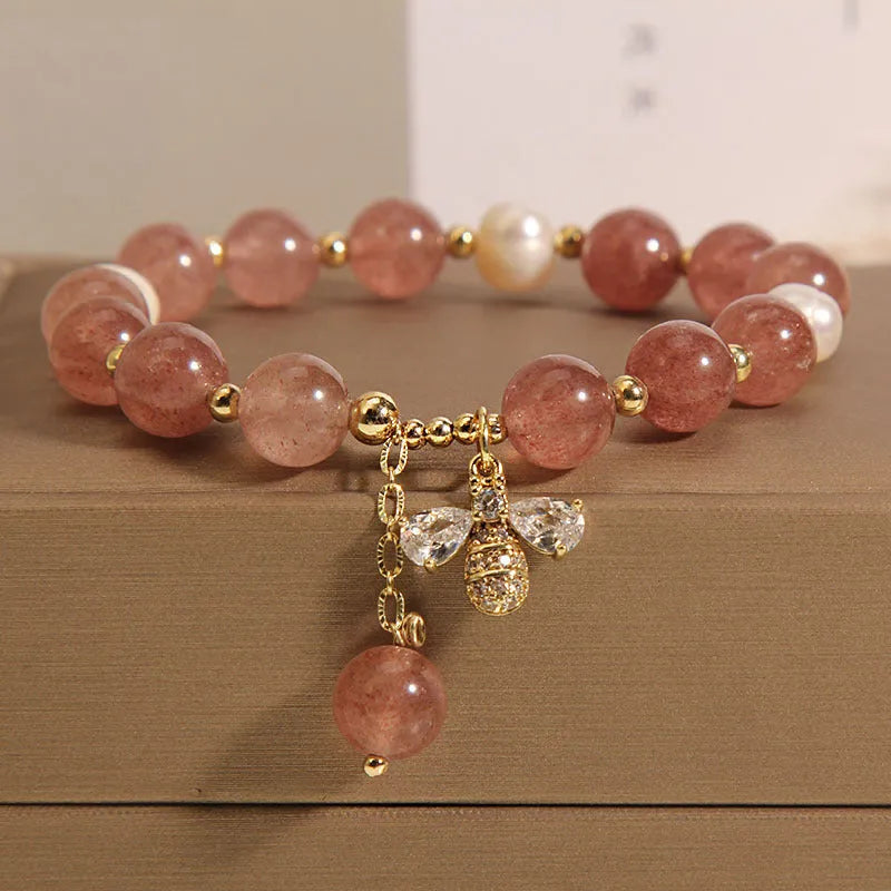 Women's pink strawberry quartz and white freshwater pearl bracelet with zircon details on wrist.
