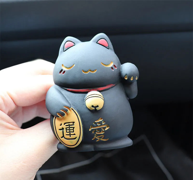 Black and white resin fortune cat ornament designed to clip onto a car air vent as an aromatherapy diffuser.
