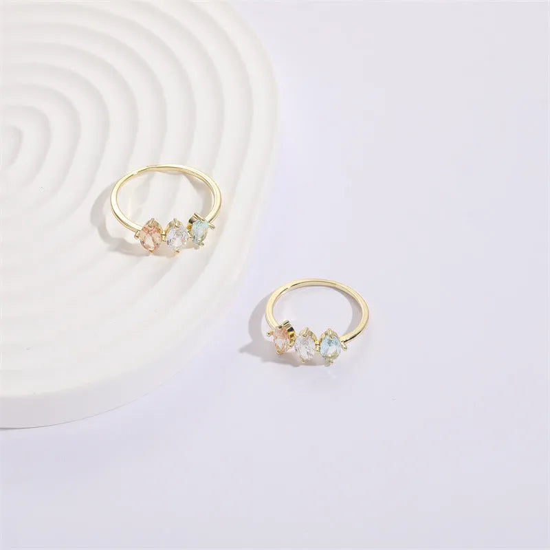 Gold colour geometric triangle ring with horse eye design and tricolour zircon stones on a white background