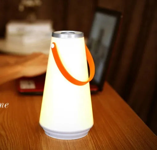 White rechargeable LED bedside lantern with USB cable on a table.