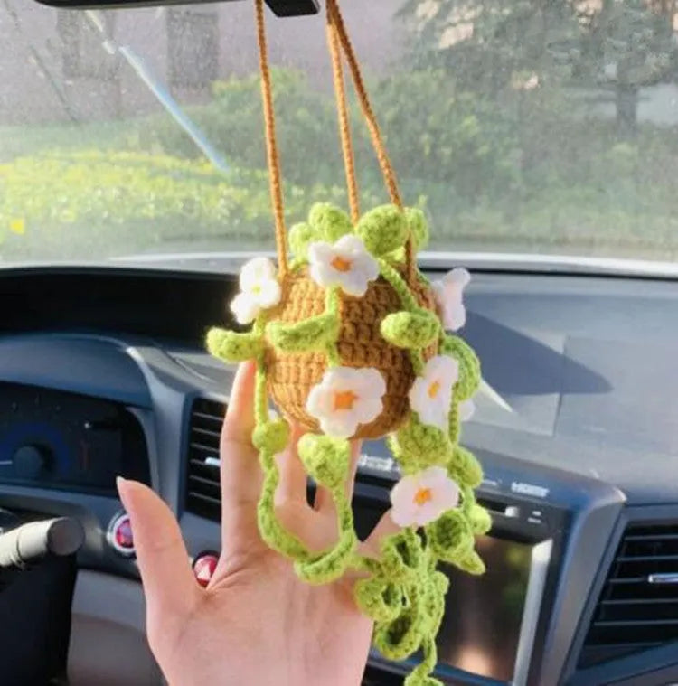 Green and white crocheted car plant decoration with hanging rope on a car dashboard.