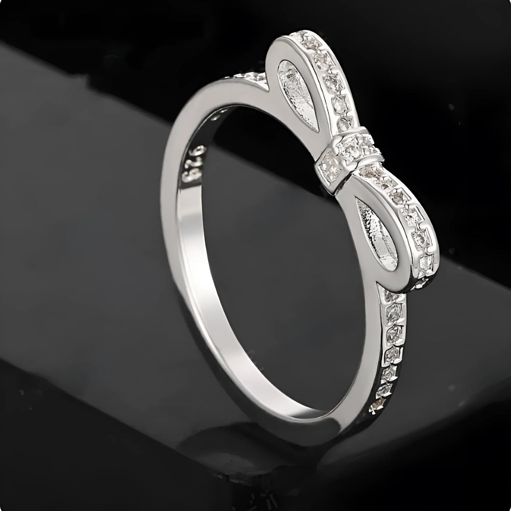 Silver bow-shaped ring with sparkling zircon crystal stones on a finger.