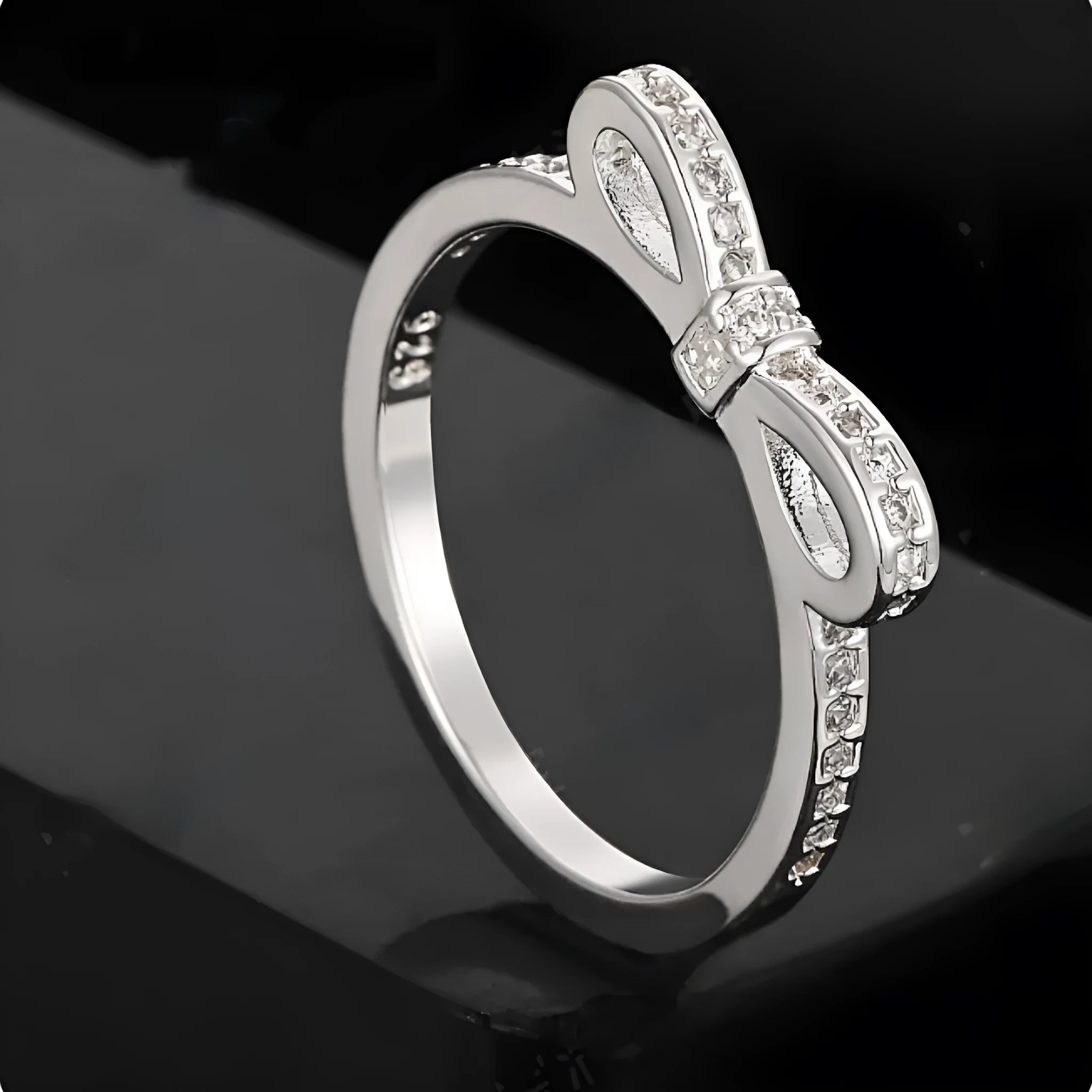 Silver bow-shaped ring with sparkling zircon crystal stones on a finger.