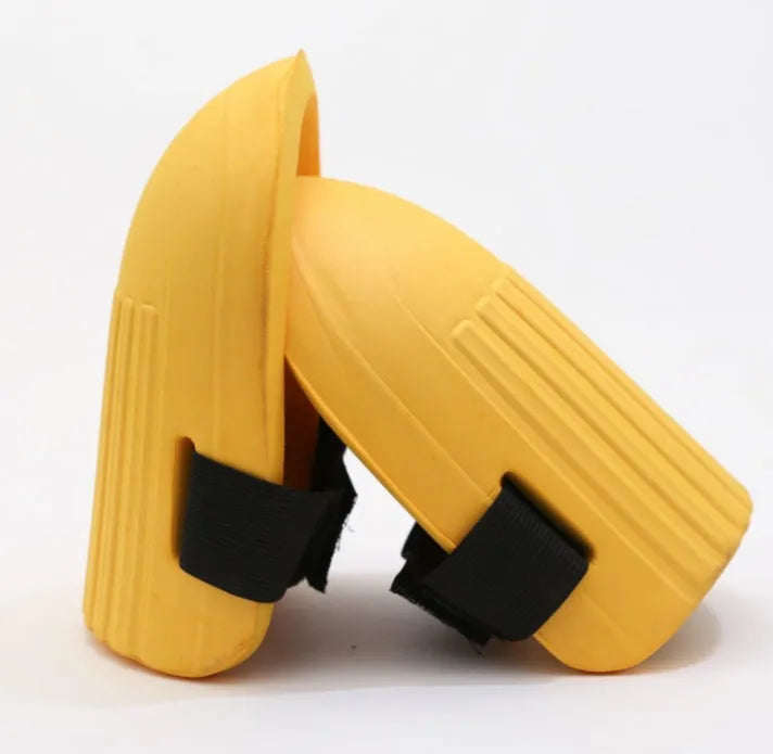A pair of EVA foam knee pads in army green colour, shown from above on a garden soil background.