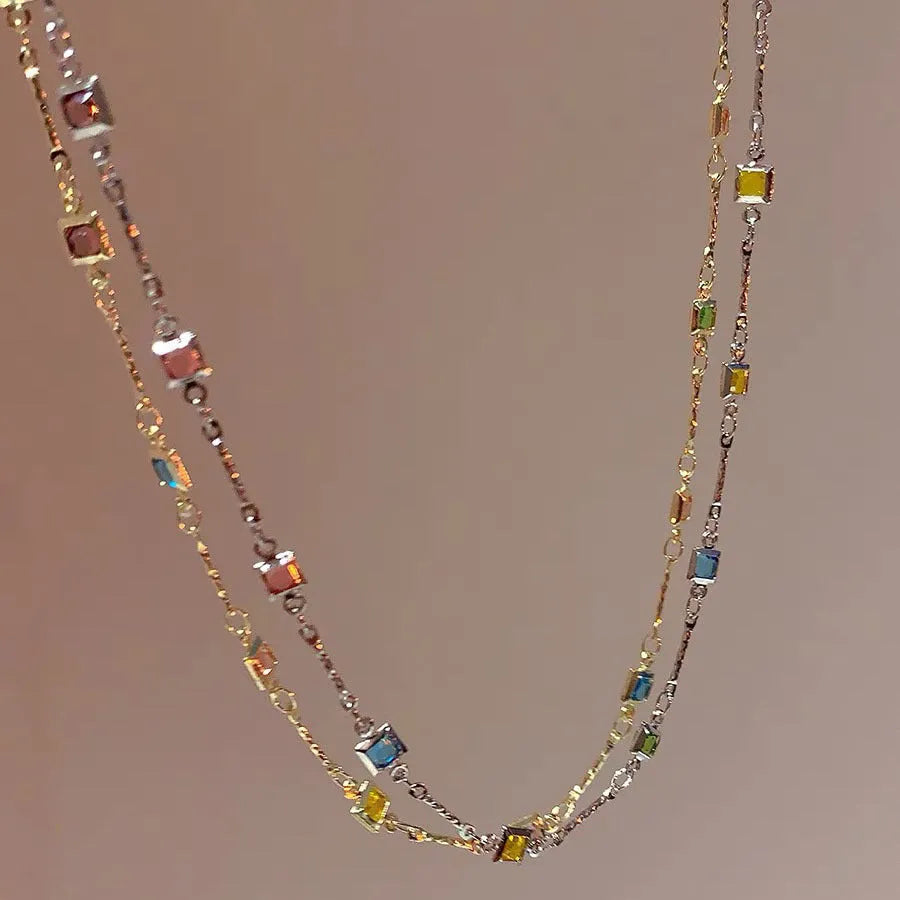Square geometric clavicle chain necklace in gold tone with artificial crystal details on a white background.