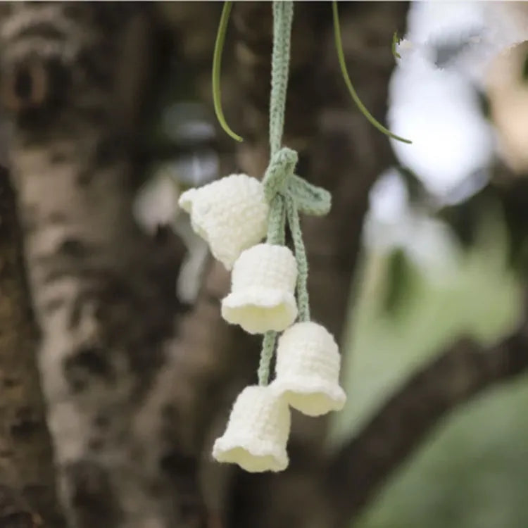 Green and white crocheted car plant decoration with hanging rope on a car dashboard.
