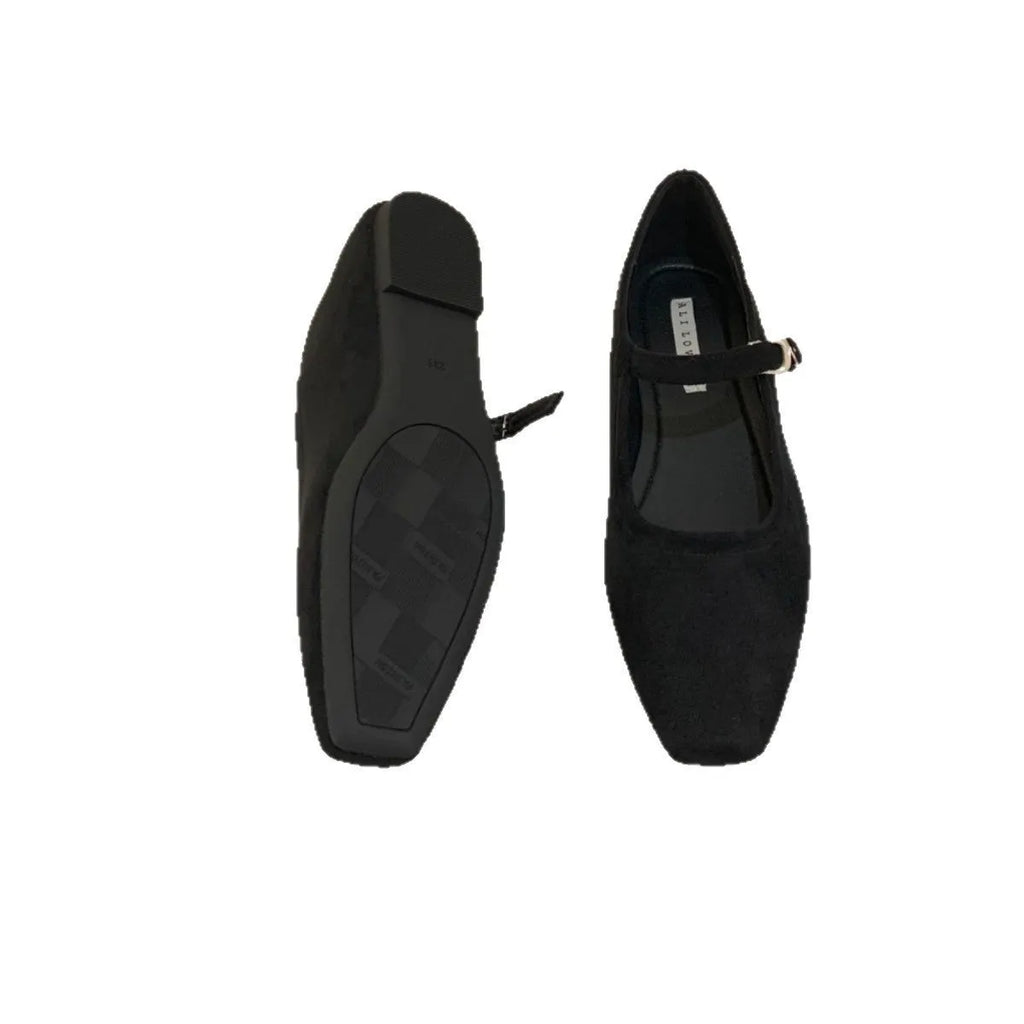 Women's black suede flat shoes with buckle closure and low heel on a neutral background