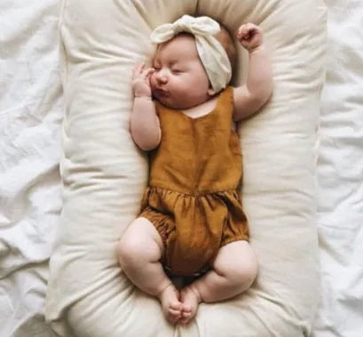 Beige portable baby nest crib cot for newborns on a neutral background.