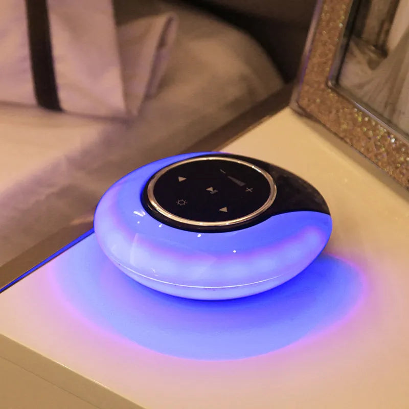 A blue and white foldable Bluetooth desk lamp with integrated speaker and touch controls on a wooden desk.