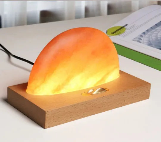 Wooden-based table lamp with a glowing orange Himalayan salt shade, wirelessly charging a mobile phone on its surface.