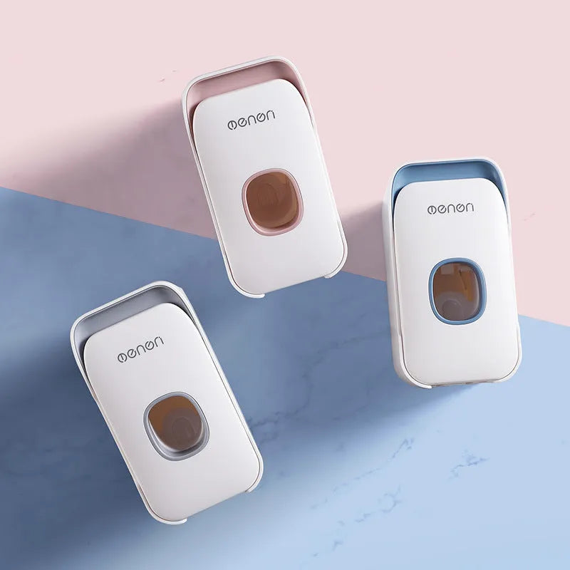 Wall-mounted automatic toothpaste dispenser in blue, grey, or pink colours with a visible dispensing lever.