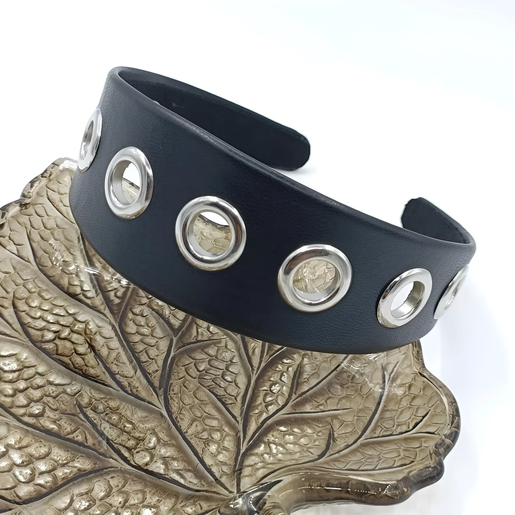 Wide black faux leather headband with round, square, and dotted rivets on a white background