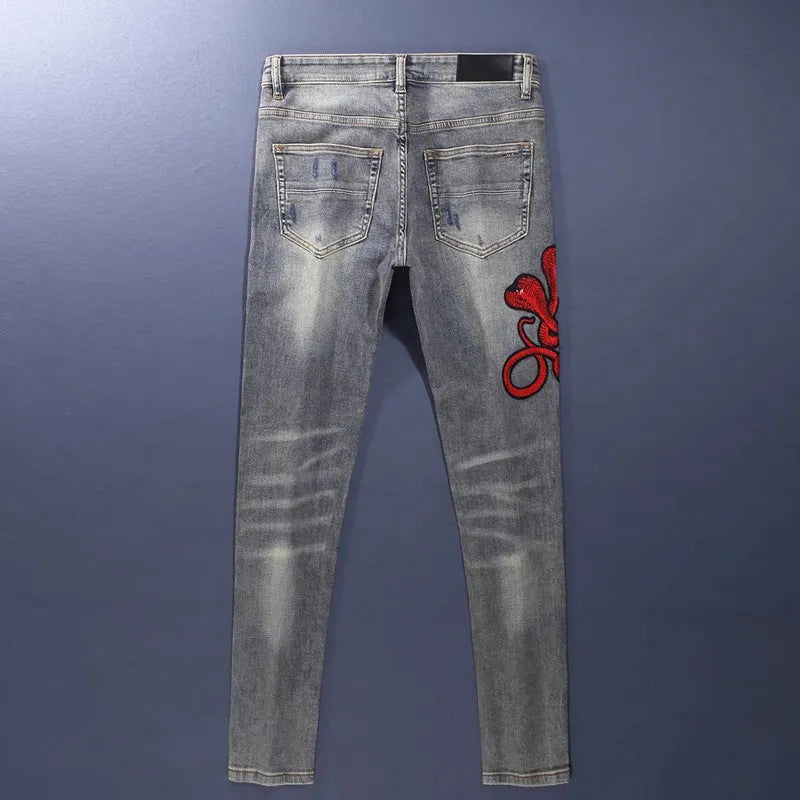 Close-up of distressed slim fit jeans showing worn wash, hole patches, and embroidery on blue denim.