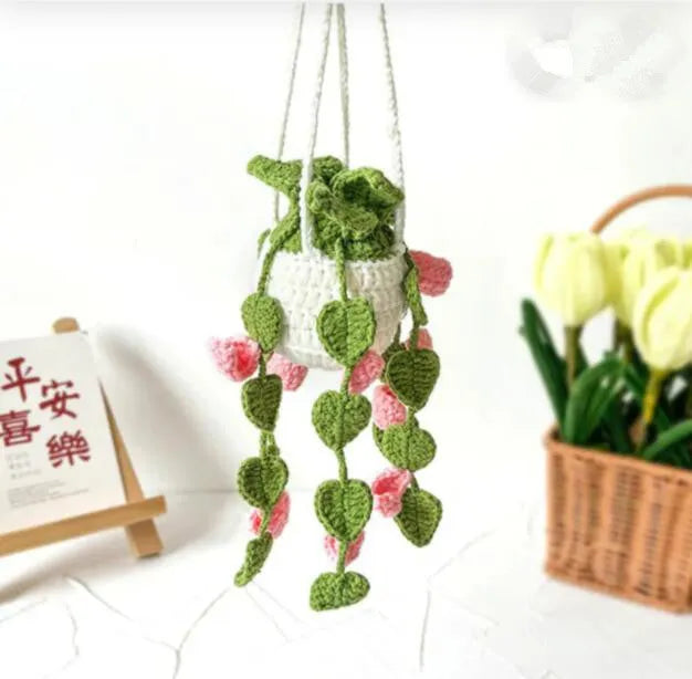 Green and white crocheted car plant decoration with hanging rope on a car dashboard.