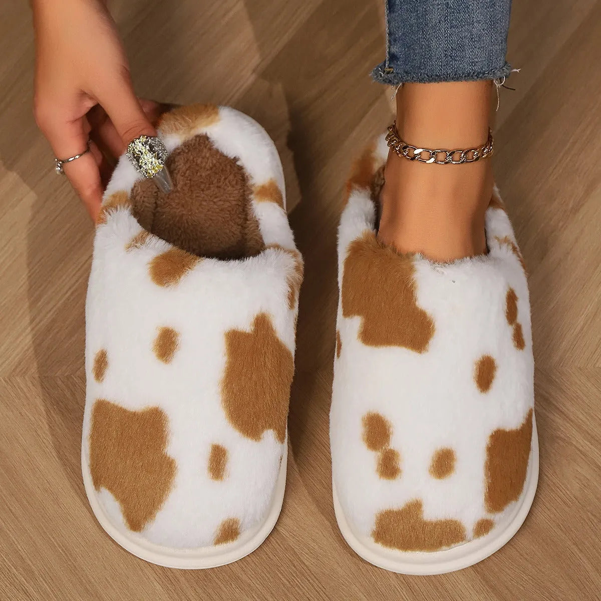 Cow spotted plush slippers in brown with round toe and baotou style on a home floor