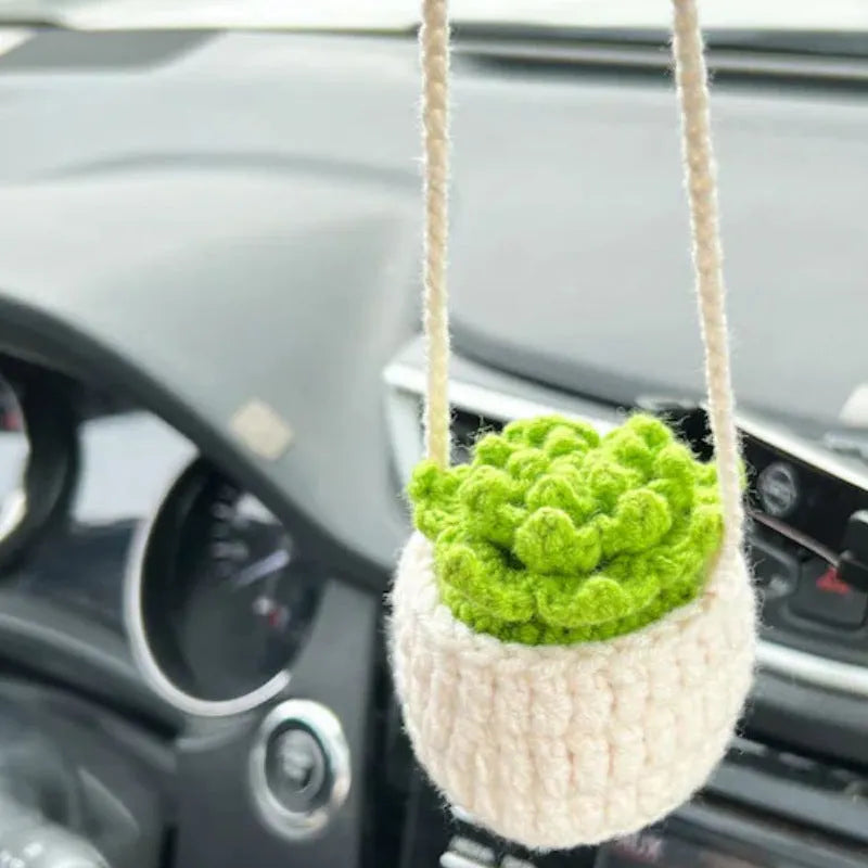 Green and white crocheted car plant decoration with hanging rope on a car dashboard.