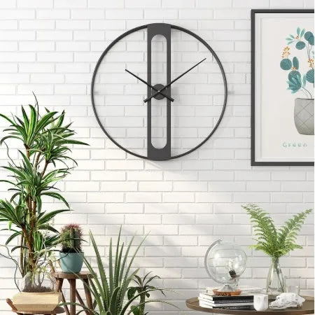 Large round metal wall clock with black dial and gold Arabic numerals on a white wall