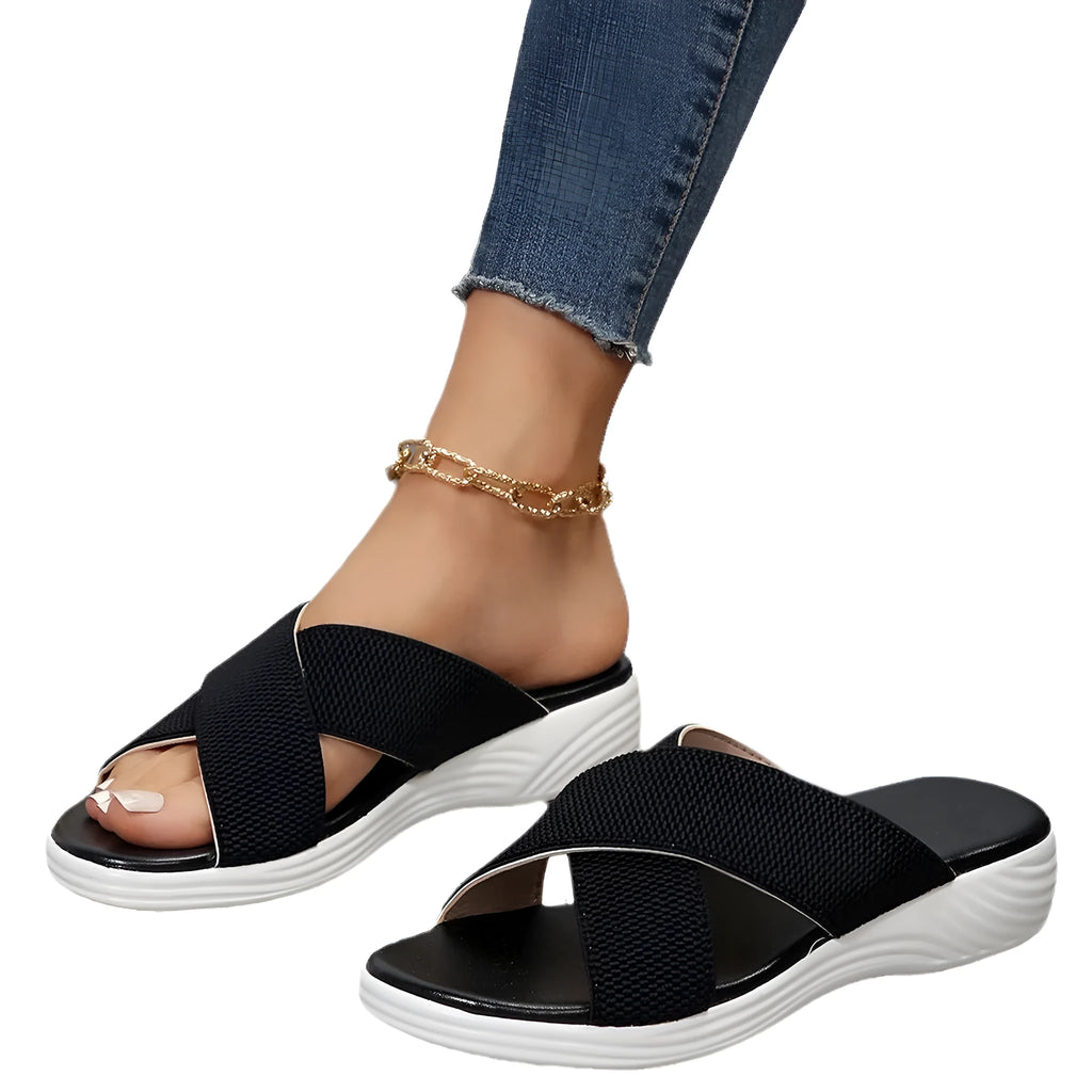 Women's black peep-toe wedge slippers with a cross strap and thick rubber sole on a grey background.