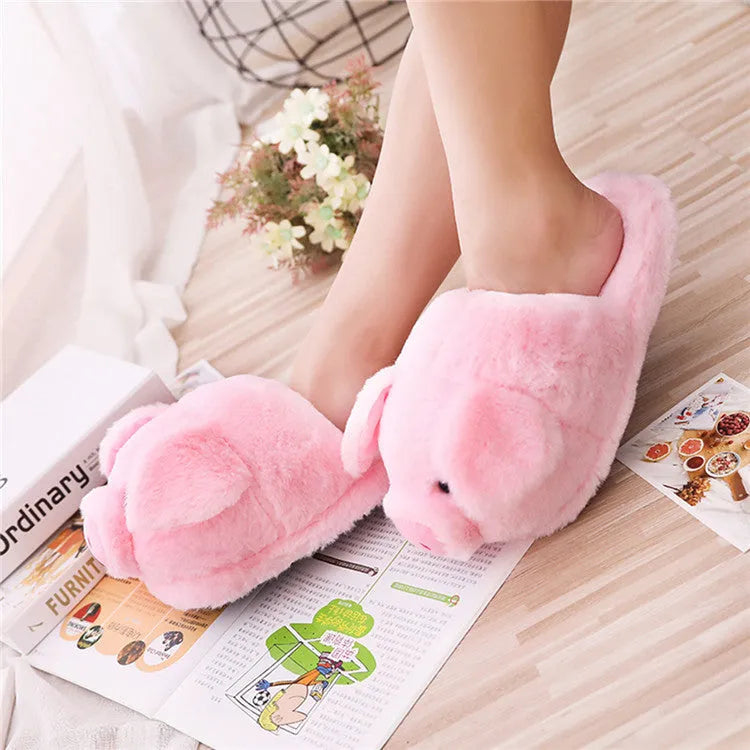 Pink pig-shaped plush floor slippers on a clean floor, showing the short plush fabric and pig design details.