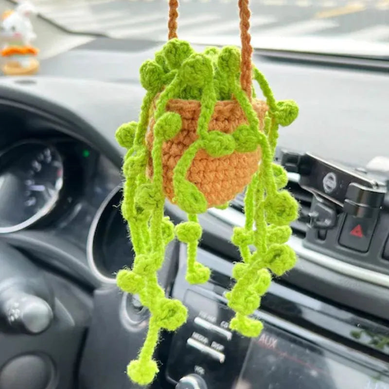 Green and white crocheted car plant decoration with hanging rope on a car dashboard.