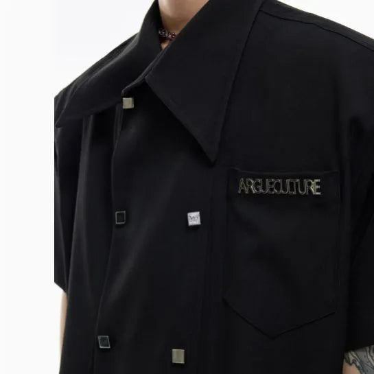 A man's loose-fit short-sleeve casual shirt with splicing detail and metal decoration on a hanger.