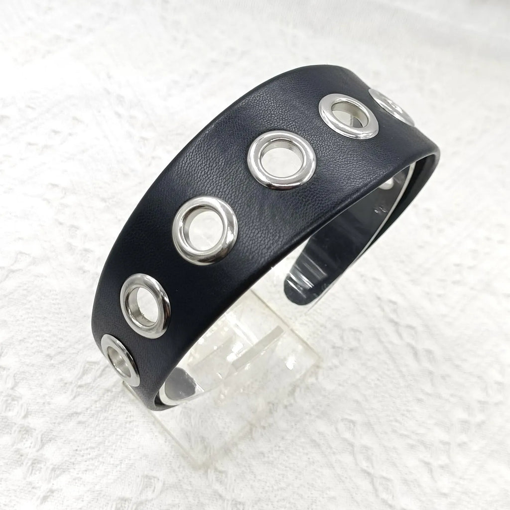 Wide black faux leather headband with round, square, and dotted rivets on a white background