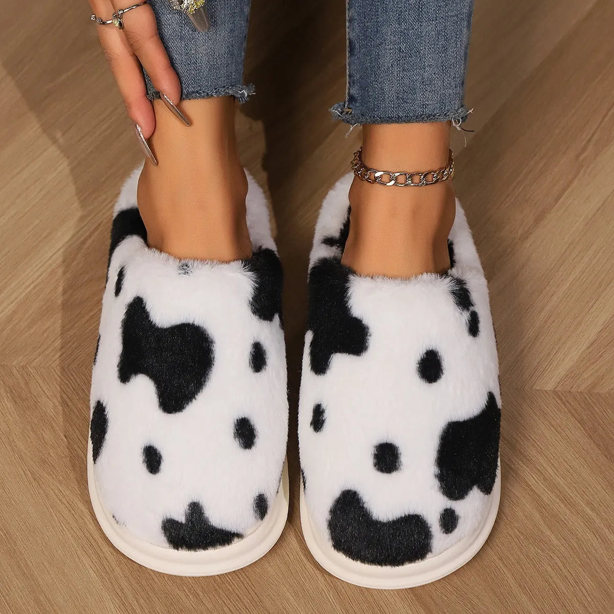 Cow spotted plush slippers in brown with round toe and baotou style on a home floor