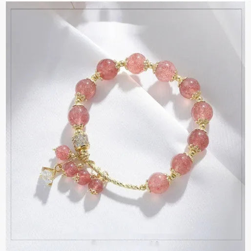 Close-up of a women's pink strawberry quartz heart bracelet with pearl details on a wrist.
