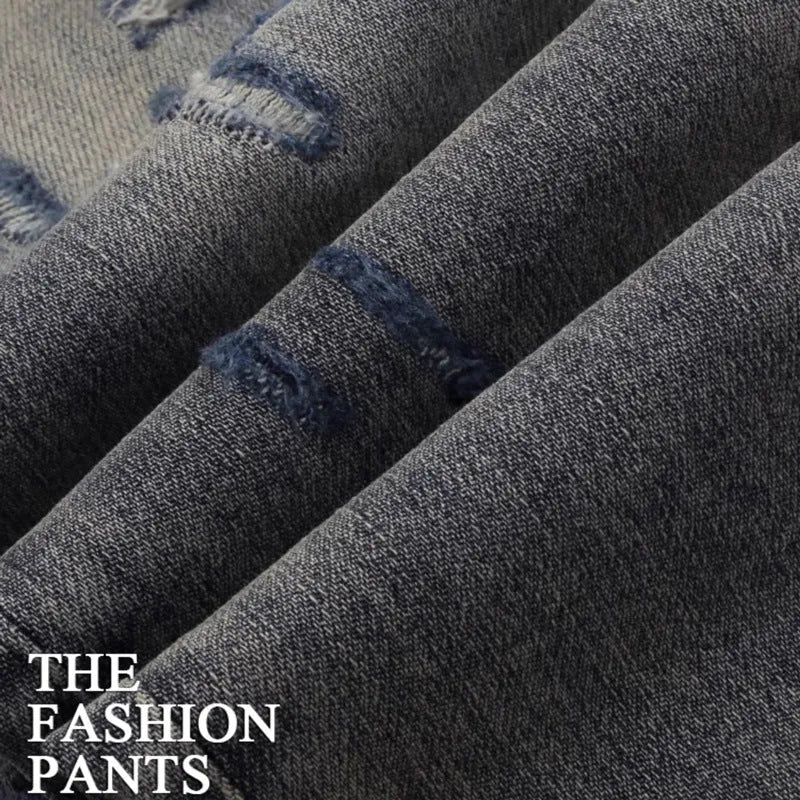 Close-up of distressed slim fit jeans showing worn wash, hole patches, and embroidery on blue denim.