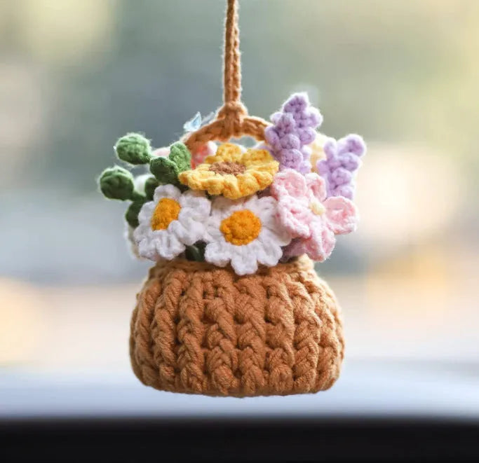 Green and white crocheted car plant decoration with hanging rope on a car dashboard.