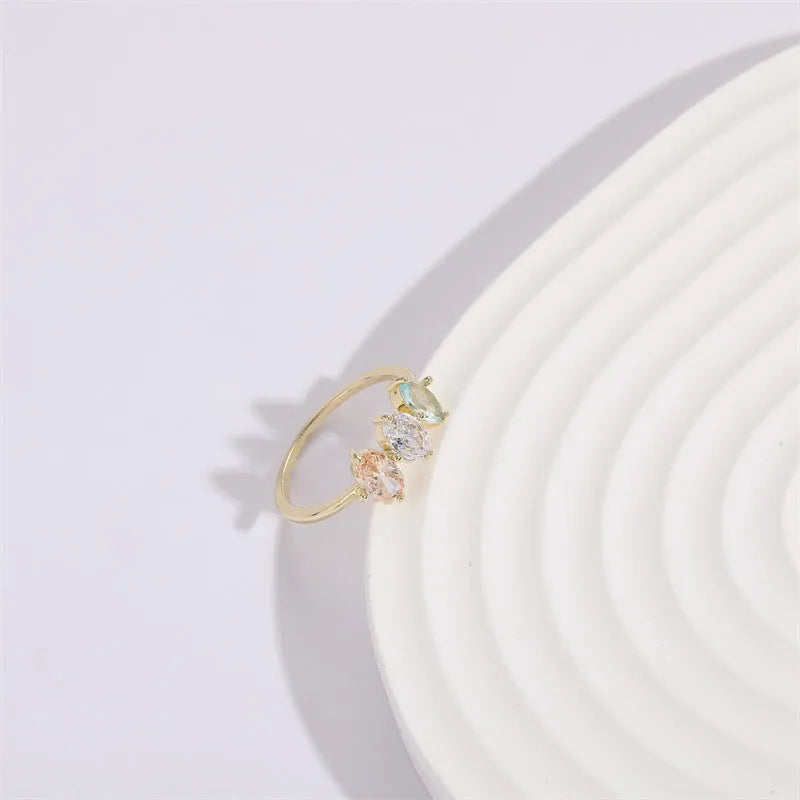 Gold colour geometric triangle ring with horse eye design and tricolour zircon stones on a white background