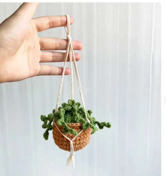 Green and white crocheted car plant decoration with hanging rope on a car dashboard.