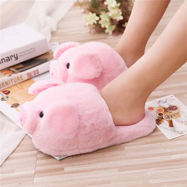 Pink pig-shaped plush floor slippers on a clean floor, showing the short plush fabric and pig design details.