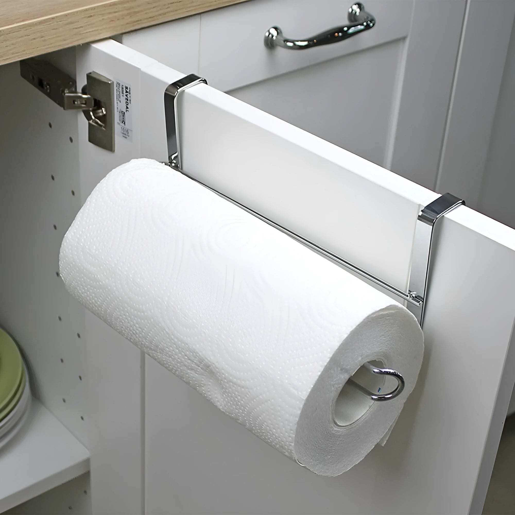 Silver stainless steel paper towel rack hanging on a kitchen cabinet door