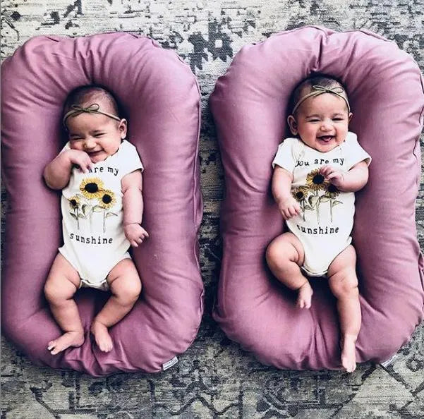 Beige portable baby nest crib cot for newborns on a neutral background.