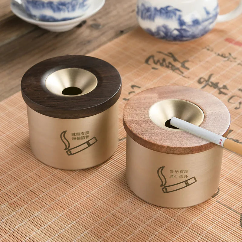 Retro-style solid copper ashtray with a wooden lid featuring a centre hole, shown in brass and black wood or brass and red wood.