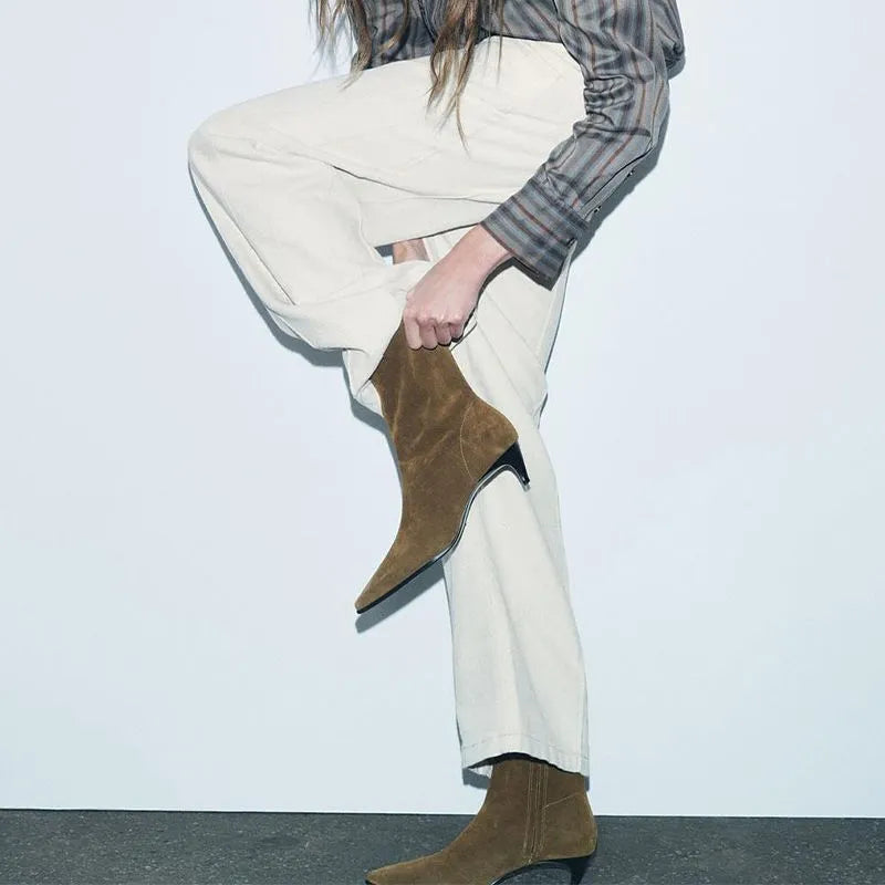 Brown square toe ankle boots with a side zipper and pointed stiletto heel on a wooden floor.