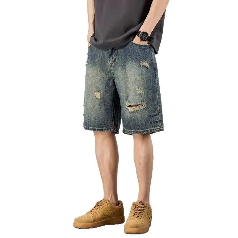 Blue men's distressed denim shorts with a loose, straight leg fit on a model.