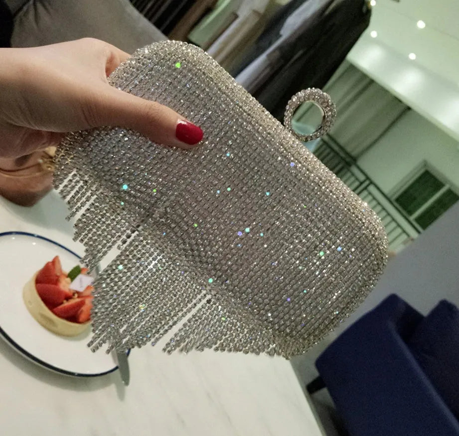 Silver ladies fringed hand bag with shiny diamond embellishments and clasp closure on a plain background