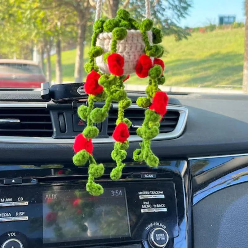 Green and white crocheted car plant decoration with hanging rope on a car dashboard.