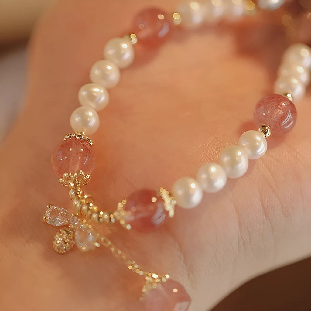 Close-up of a women's hand-strung strawberry quartz crystal bracelet with a decorative bow.