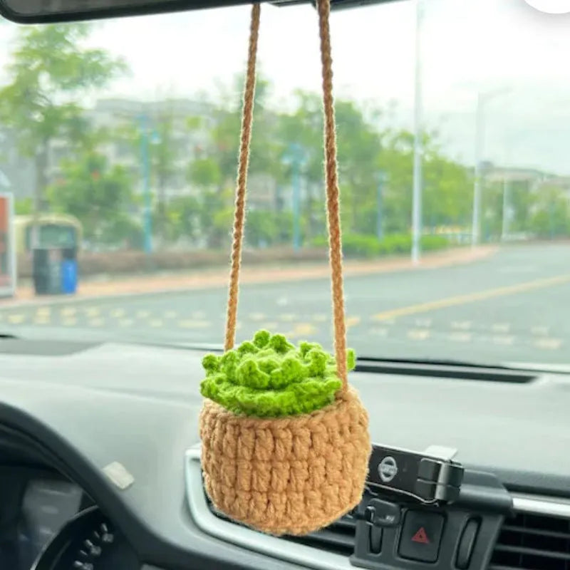Green and white crocheted car plant decoration with hanging rope on a car dashboard.