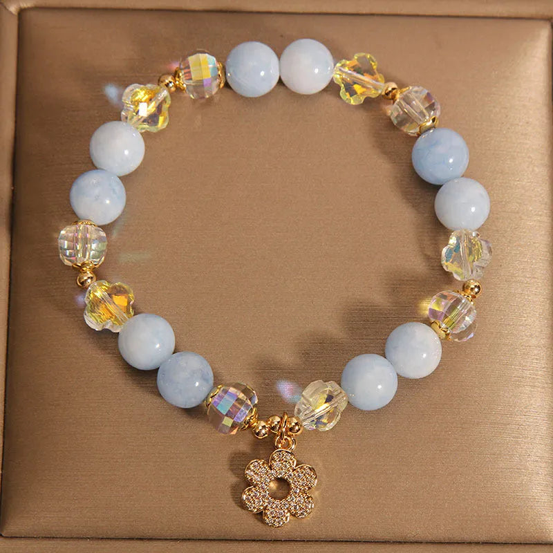 Aquamarine crystal bracelet with four-leaf clover charm and pearl detail on a wrist.