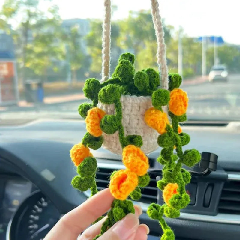 Green and white crocheted car plant decoration with hanging rope on a car dashboard.